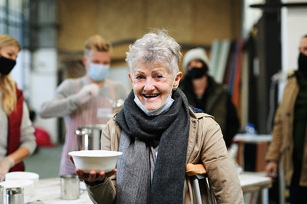 Freiwillige servieren heiße Suppe. Eine ältere Frau hat eine Suppenschüssel in der Hand.